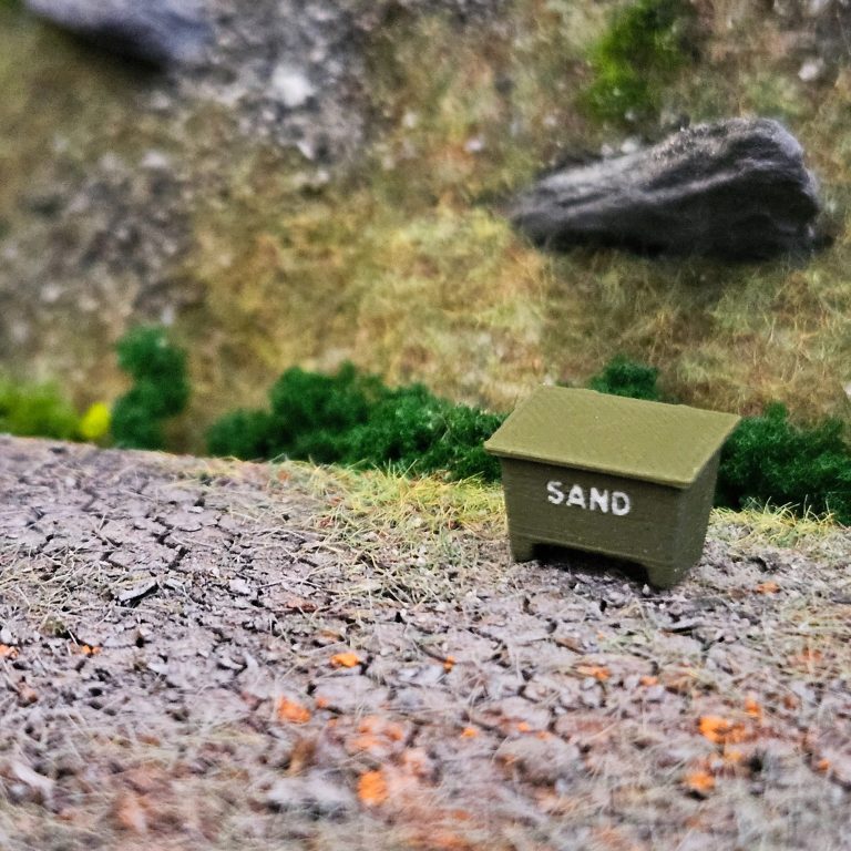 Flera godsvagnar med last av trä, kol och säckar på en modelljärnväg.